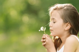 Niña soplando una flor de diente de león en un entorno natural, representando pureza, salud natural y bienestar