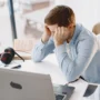 Hombre sentado frente a un computador mostrando signos de estrés y agotamiento mientras trabaja desde casa.