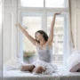 Mujer estirándose al despertar en su habitación, representando descanso, relajación muscular y bienestar diario.