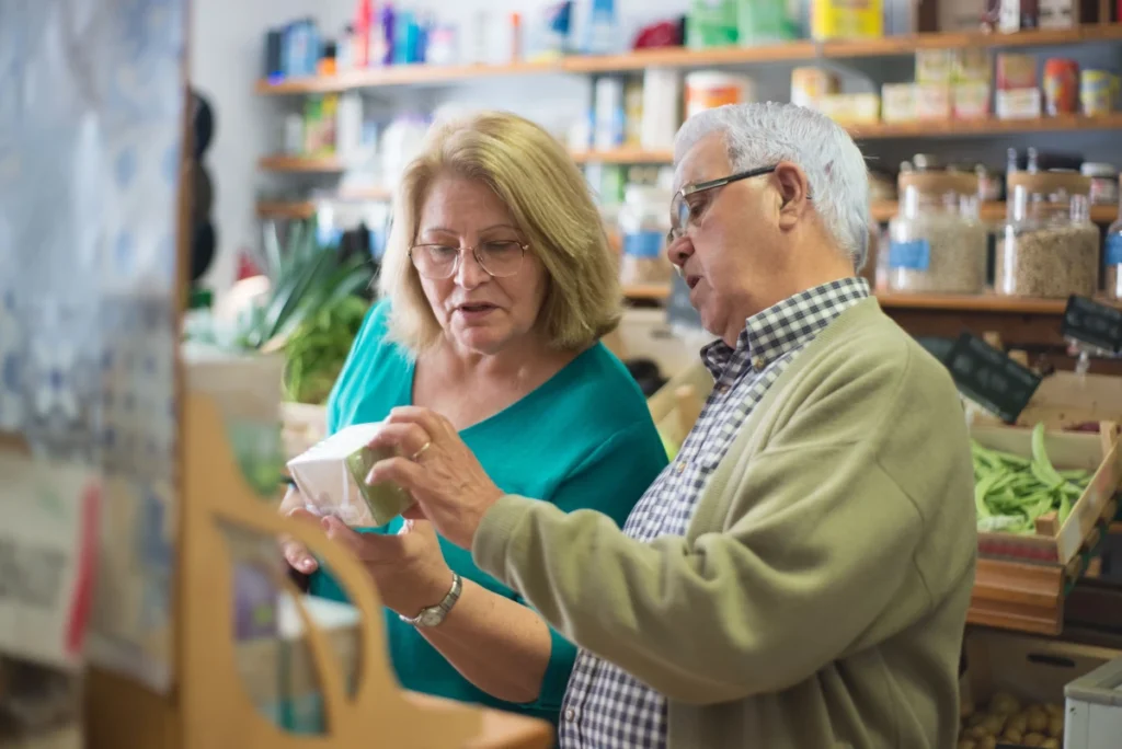 Pareja de adultos mayores revisando la etiqueta de un suplemento nutricional en una tienda especializada